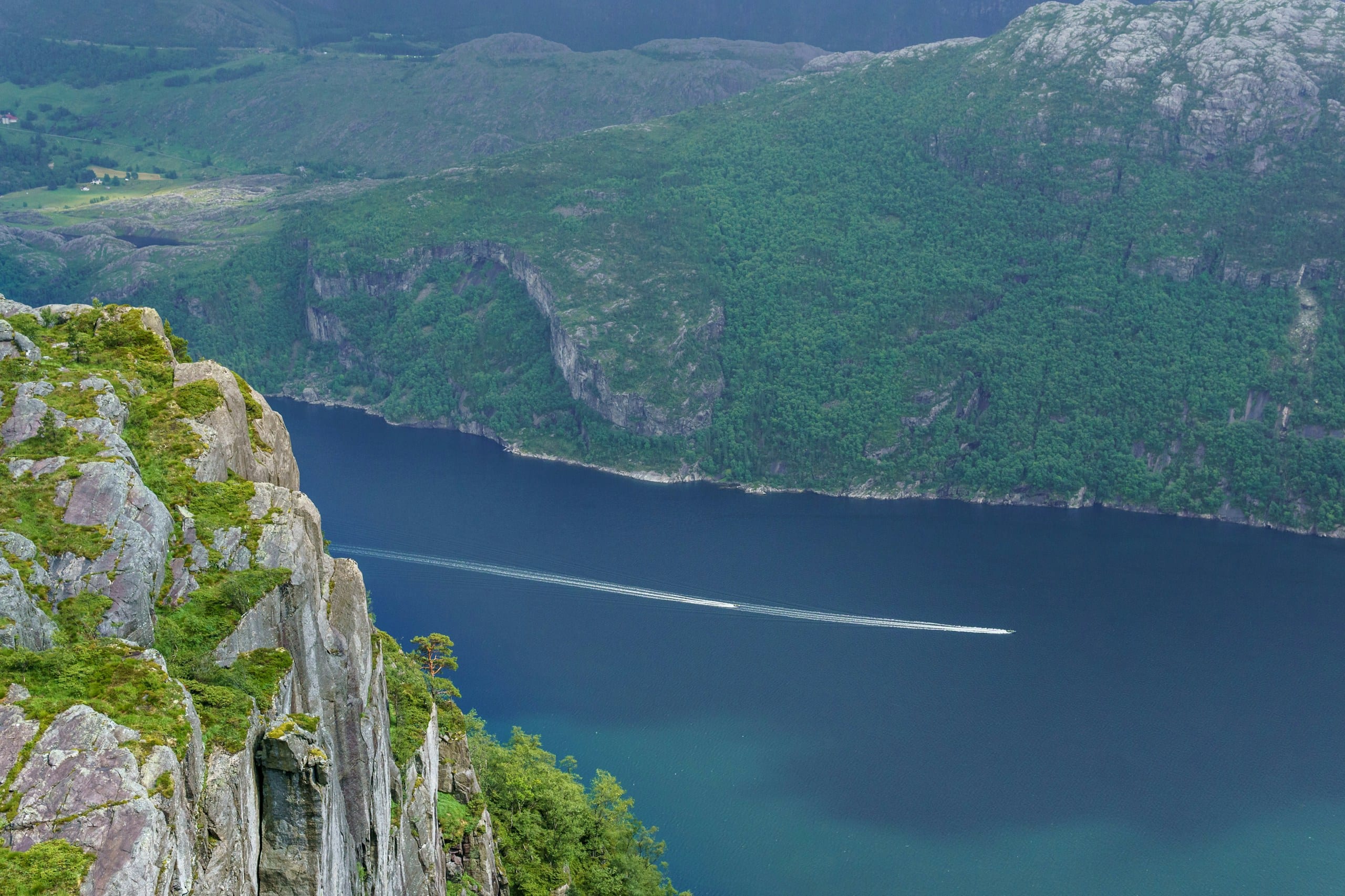 A boat crossing a wide Norwegian fjord with steep forested mountains rising on both sides under a cloudy sky