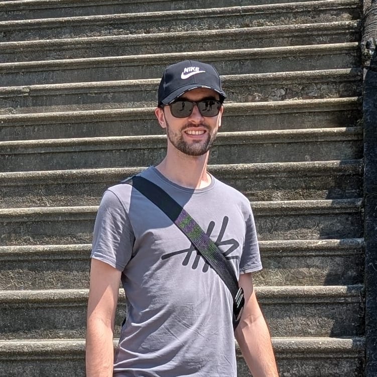Erik standing on weathered stone steps outdoors, wearing a cap and sunglasses