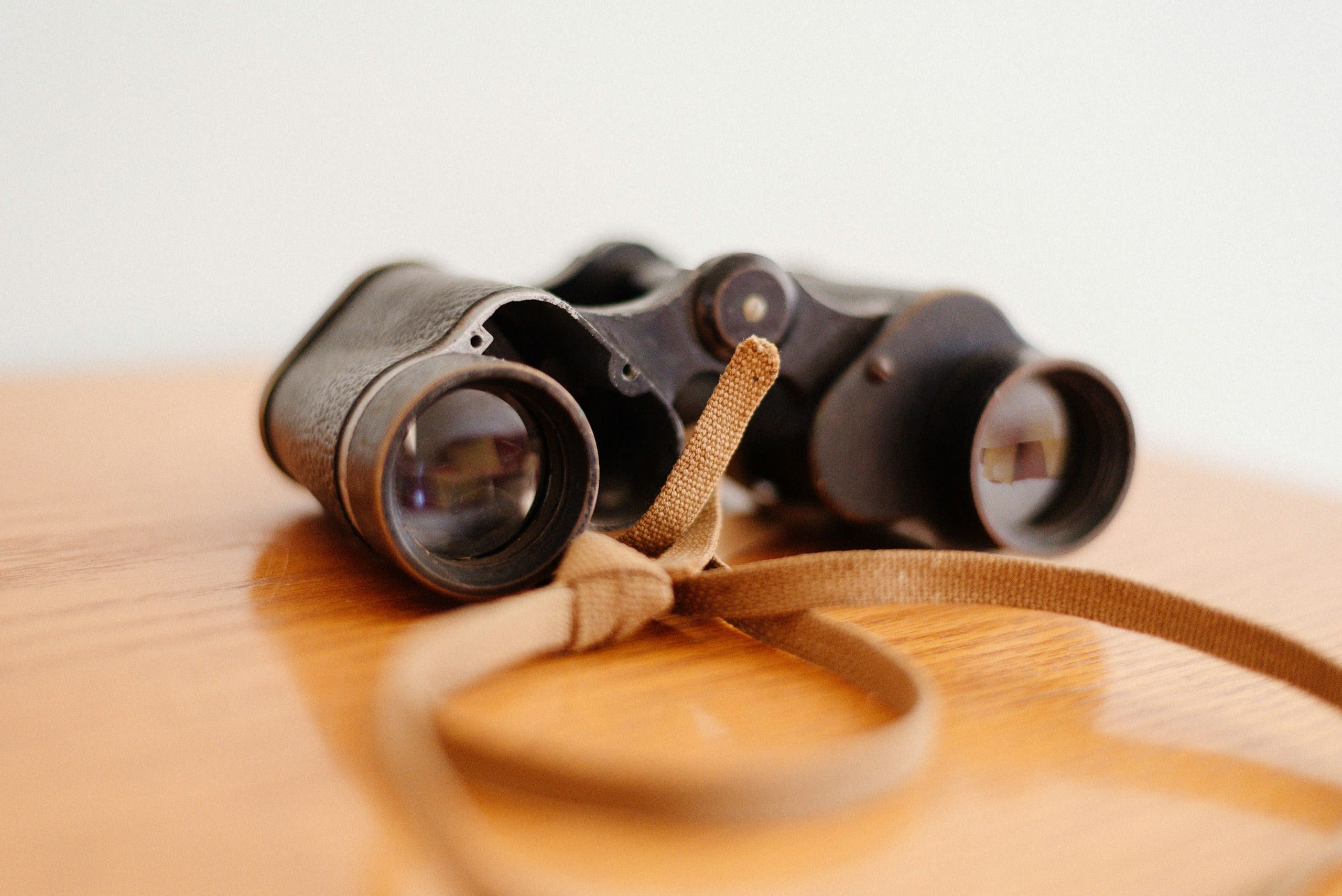 A pair of compact roof-prism binoculars resting on a wooden surface, lens caps open