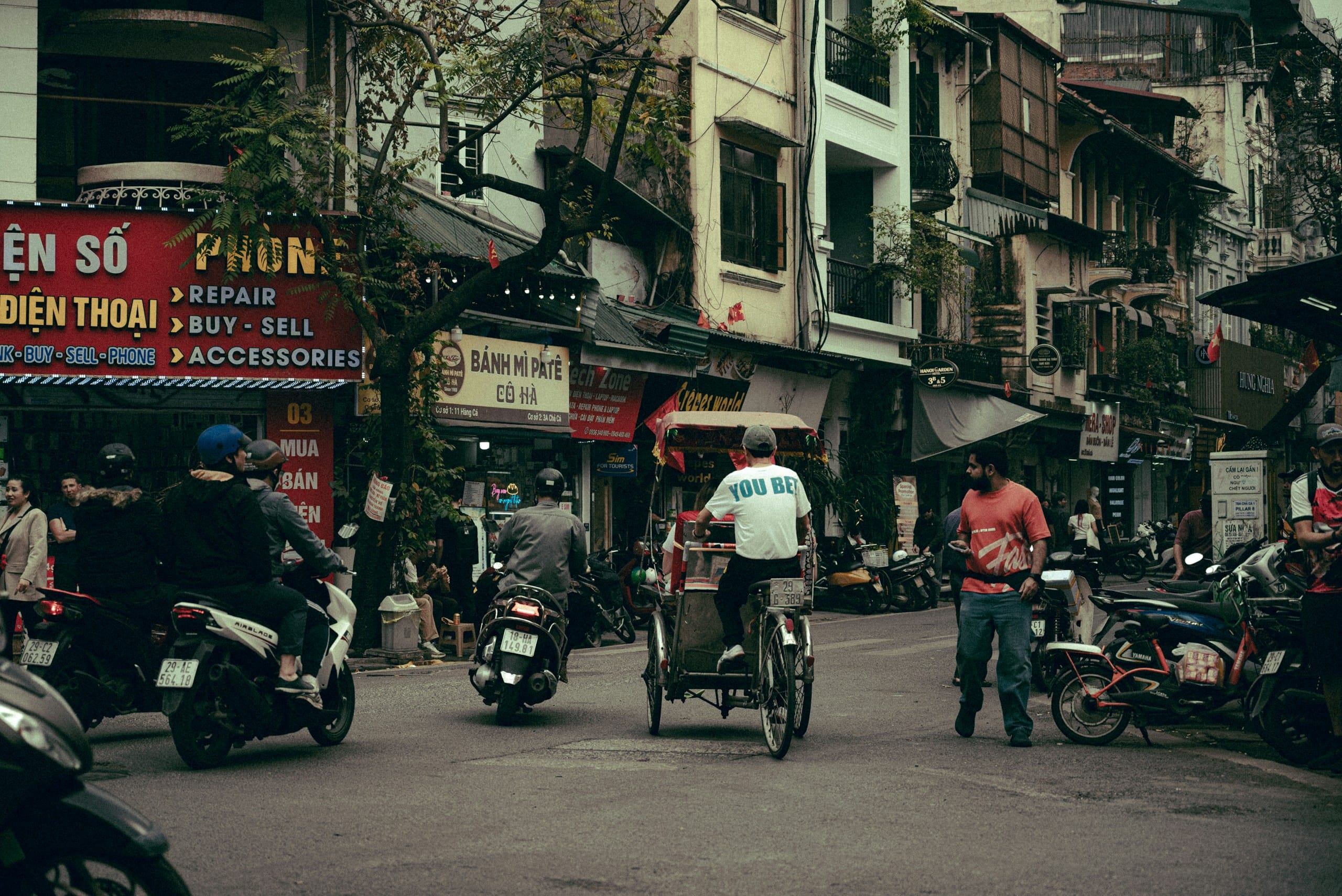 A busy street in Hanoi's Old Quarter with motorbikes, cyclists, and narrow shopfronts