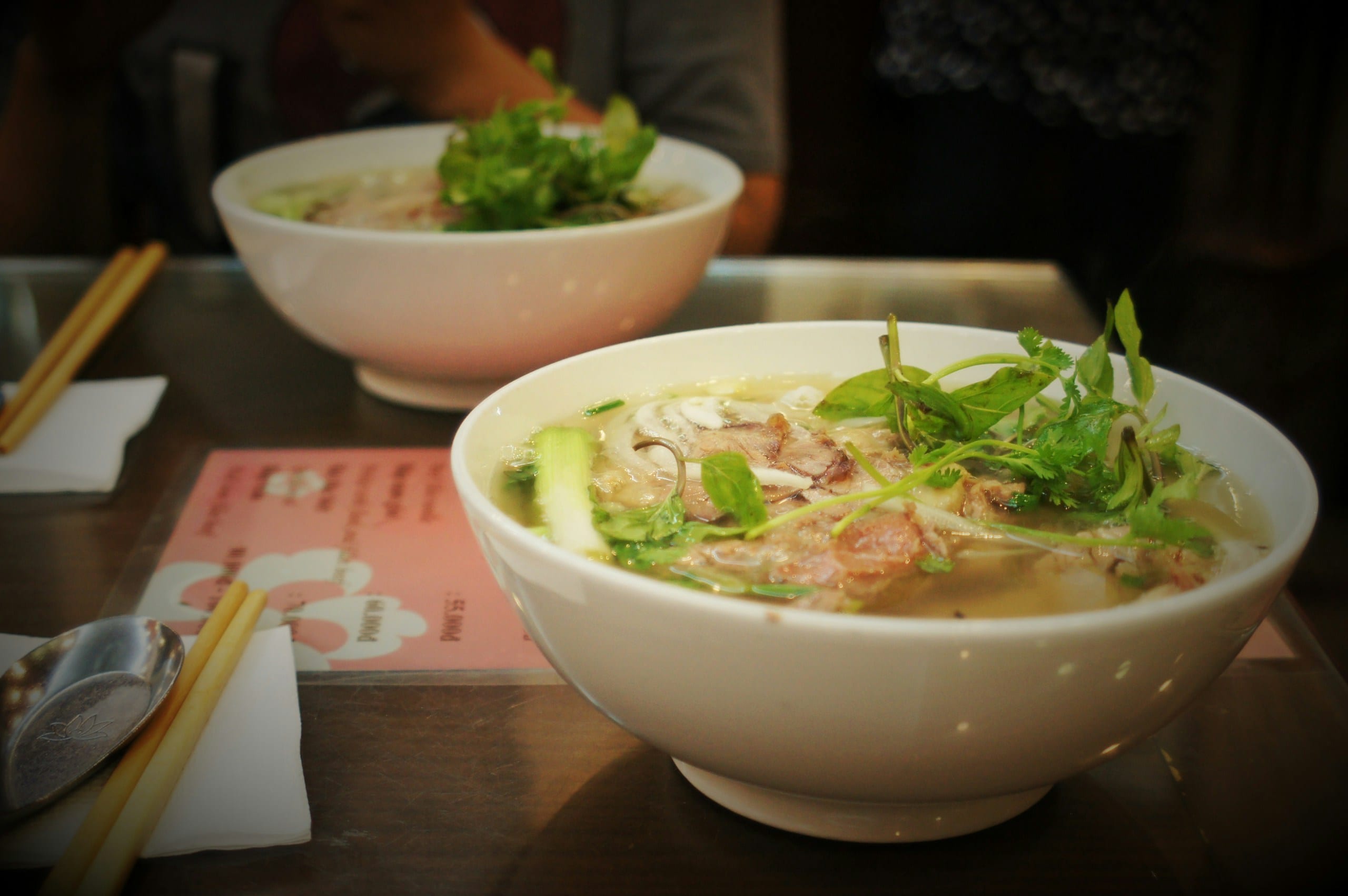 Two bowls of pho with herbs and condiments on a table in Hanoi
