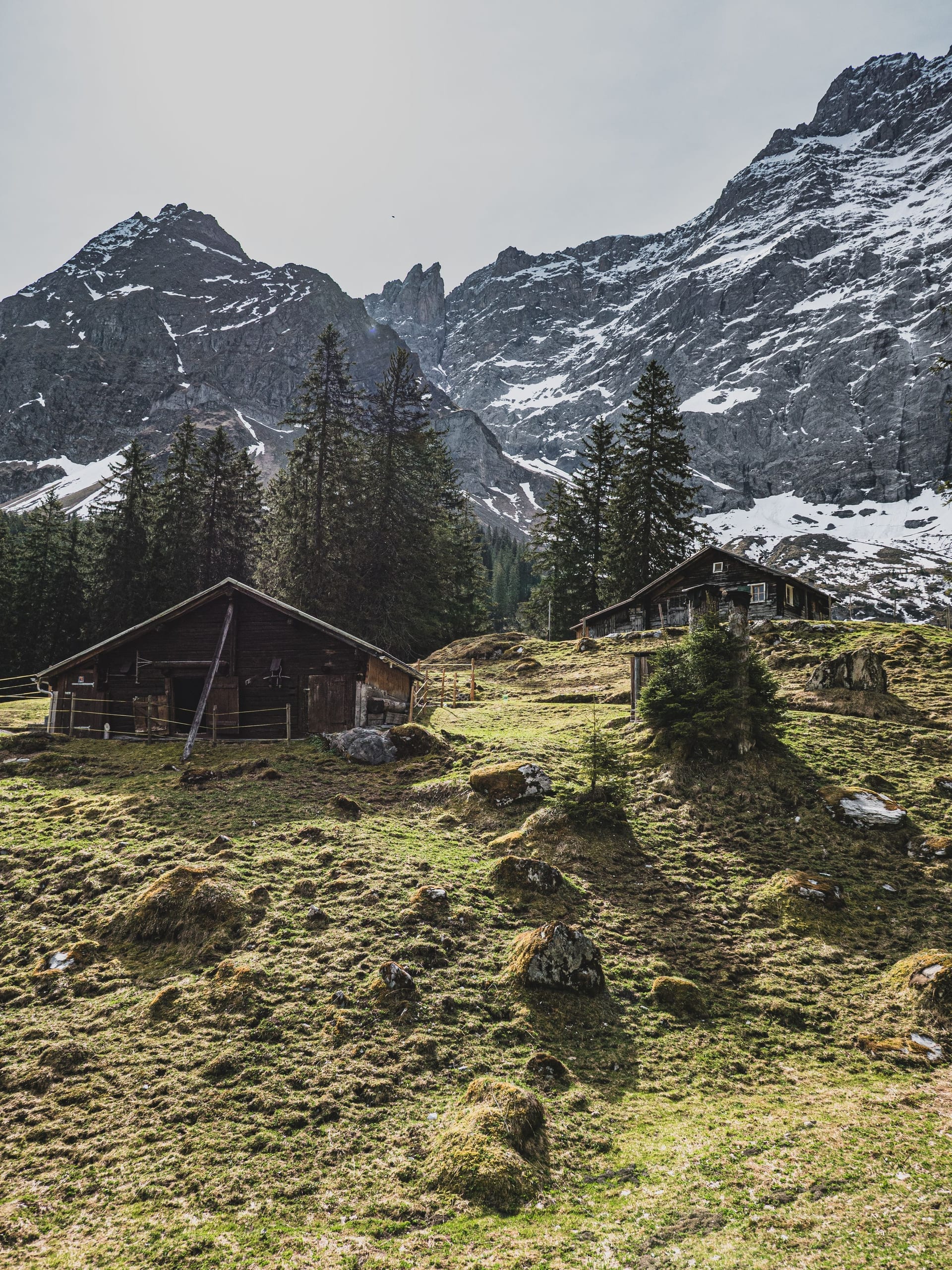 A stone-and-timber mountain hut perched on a rocky saddle high in the Alps, with peaks rising behind it