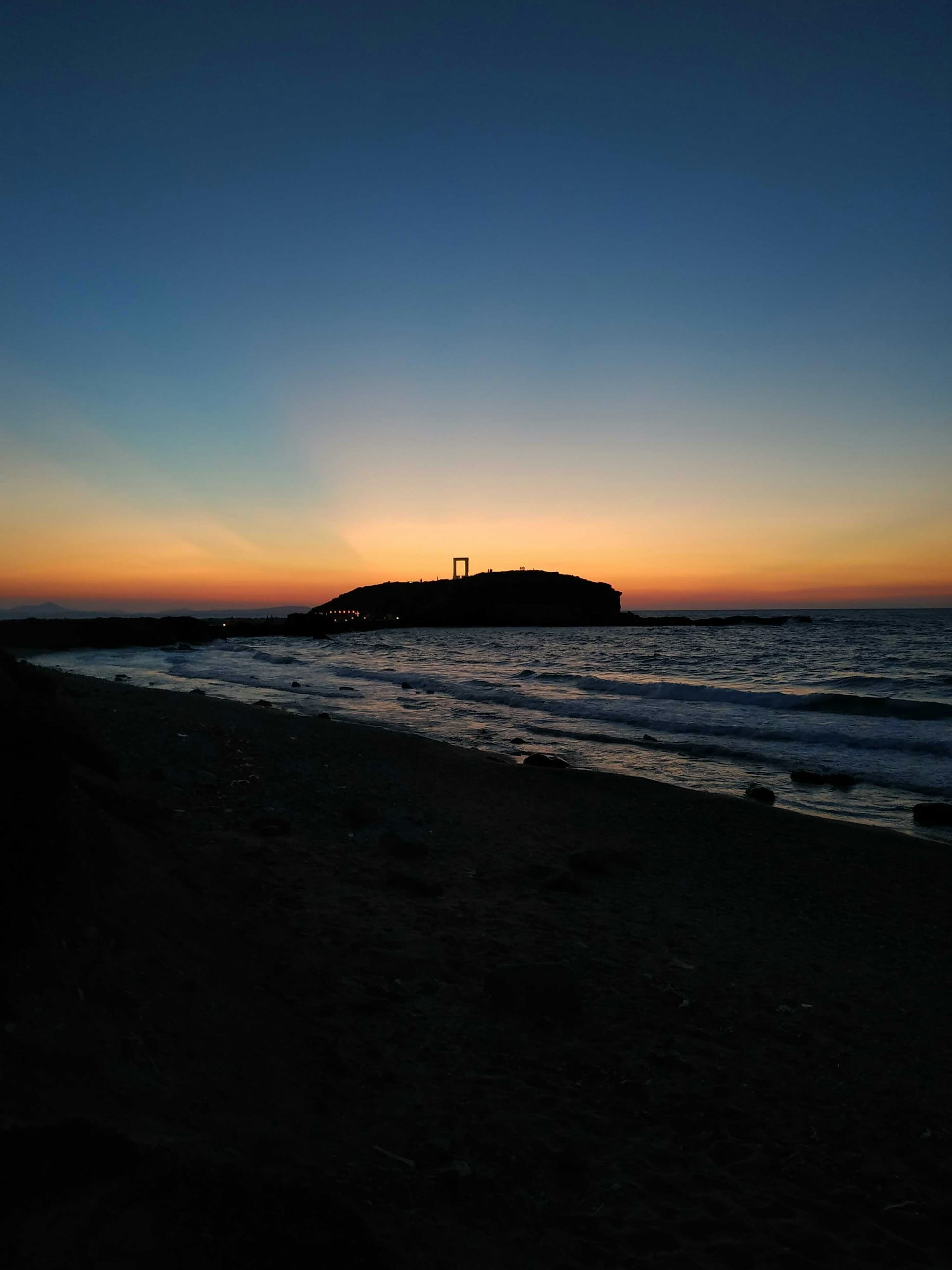 The marble Portara gateway on Naxos silhouetted against a golden sunset sky over the Aegean