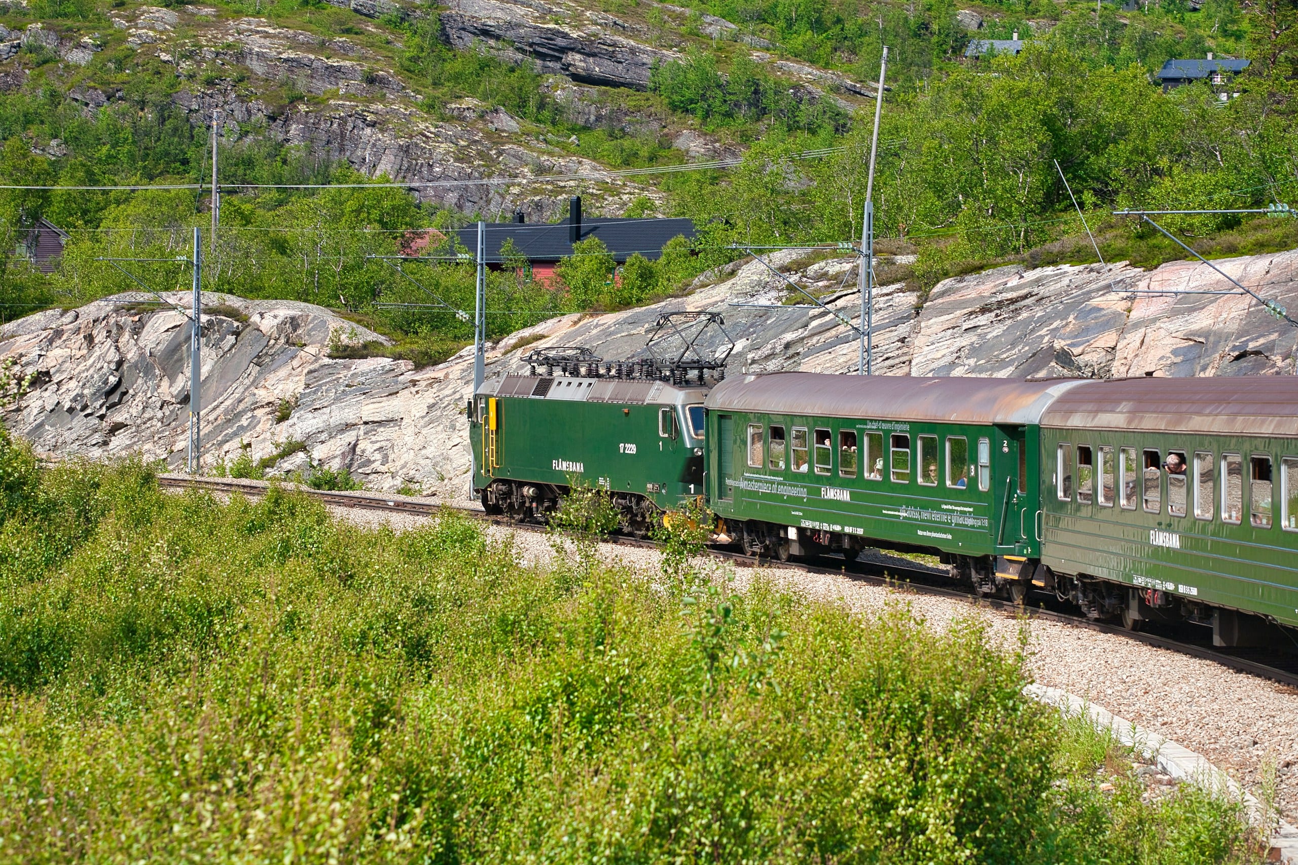 The green Flåm Railway train on tracks through a green mountain valley in western Norway