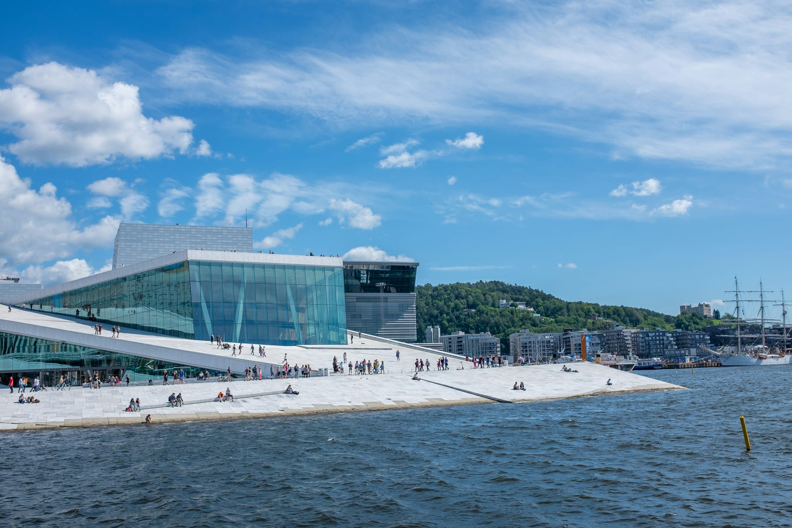 People sitting and walking on the sloped marble plaza beside Oslo's Opera House and the fjord