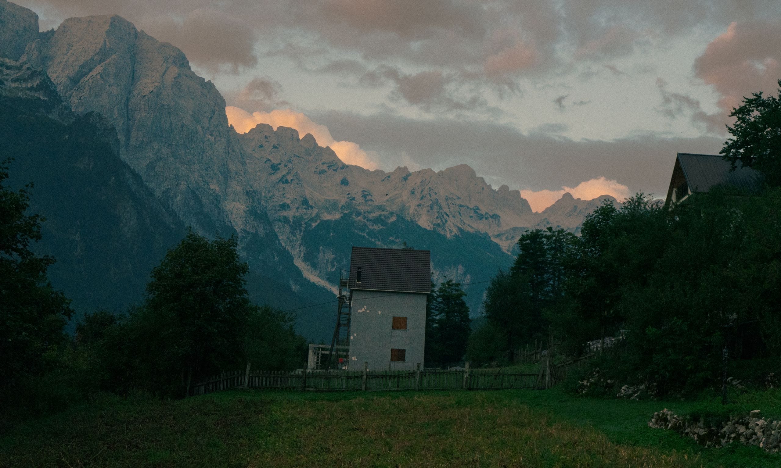 A green glacial valley framed by sharp limestone peaks in the Albanian Alps, with a river running through the floor