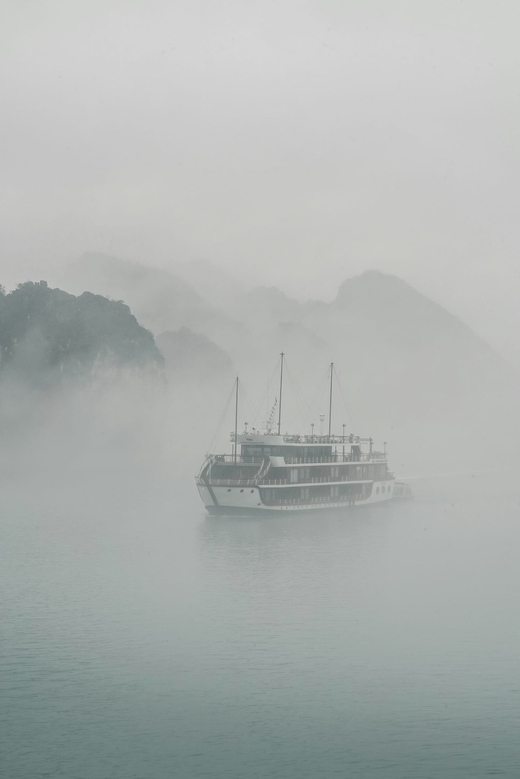 A sightseeing boat moving through fog on Ha Long Bay between limestone cliffs